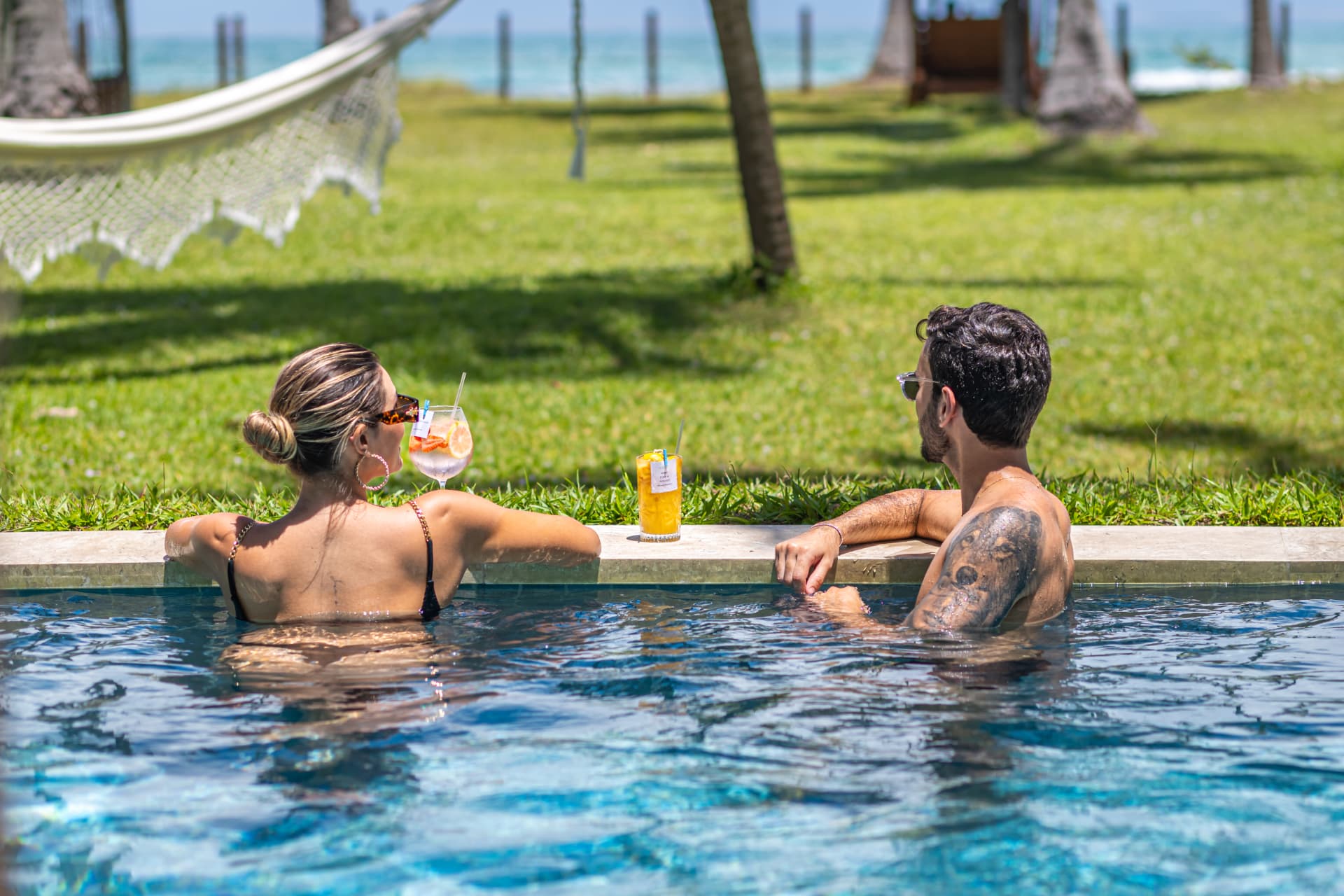 Casal na piscina com drinks e vista para o coqueiral